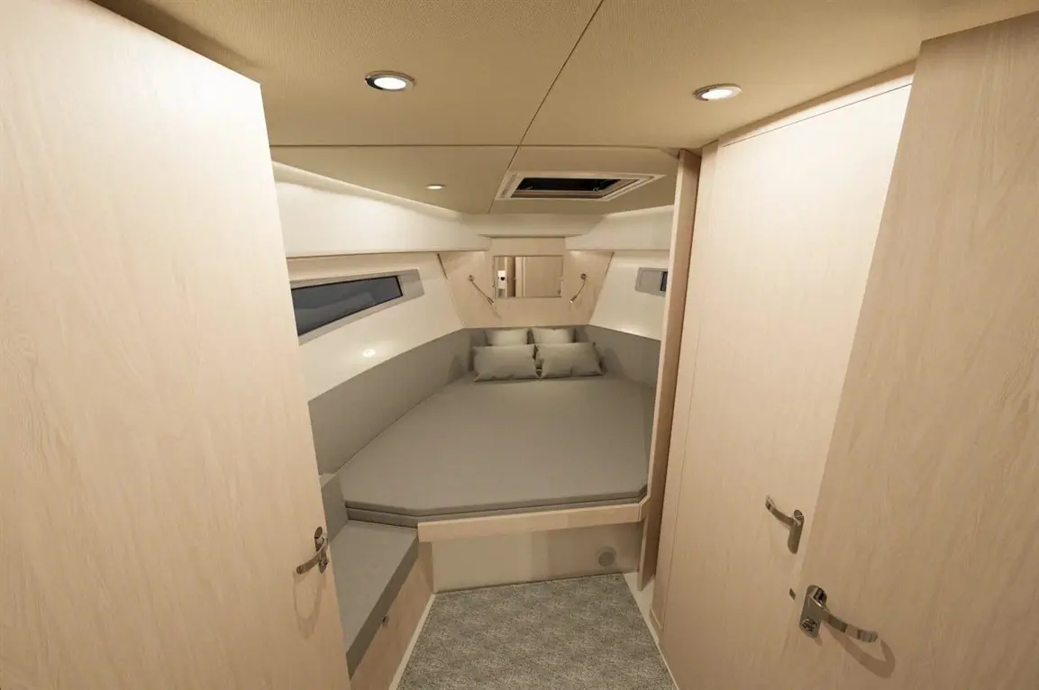 Cozy boat cabin featuring a round bed with gray cushions, wood paneling, and dual doors, illuminated by ceiling lights.